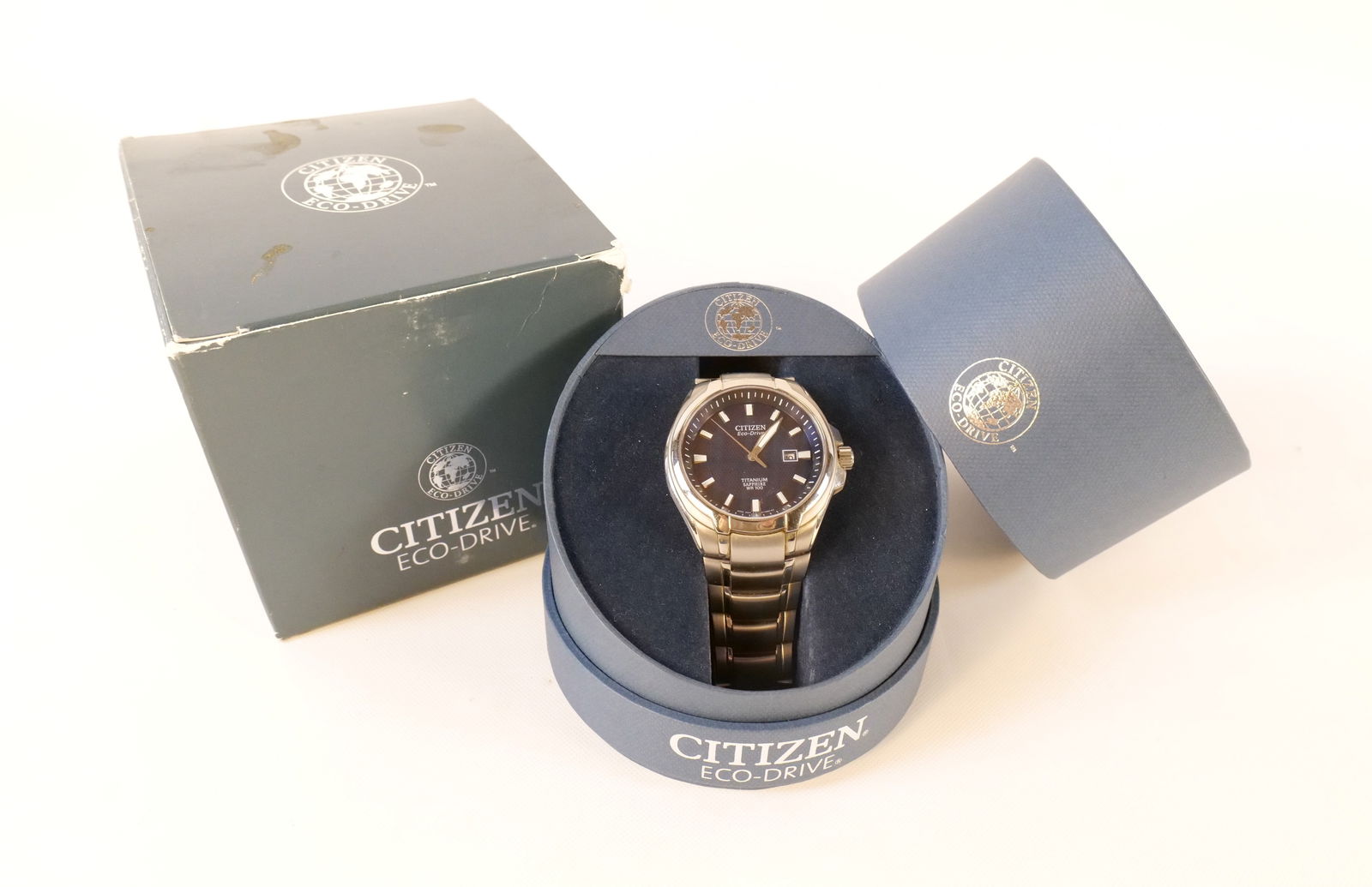 Citizen Men's Eco-Drive Blue Titanium Solar Powered Watch: Citizen Men's Eco-Drive Blue Titanium Solar Powered Watch. Sapphire Crystal. Date Window. Luminous Hands. Missing watch holder arm from inside box. Comes with outer box. Scratches and wear to band. No