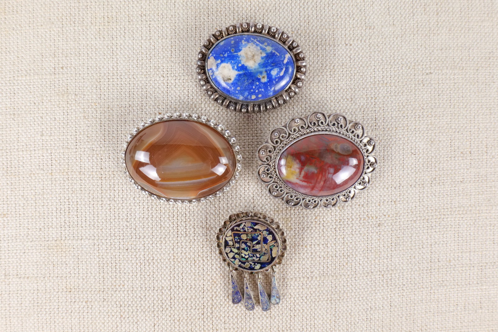 Lot of Sterling and Natural Stone Pins: Lot of sterling and natural stone pins. Includes an agate pin, a Lapis lazuli pin, a Mexican sterling inlaid pin/pendant and one unidentified stone pin. The Hins measure between 1 1/4" and 1 3/4". All