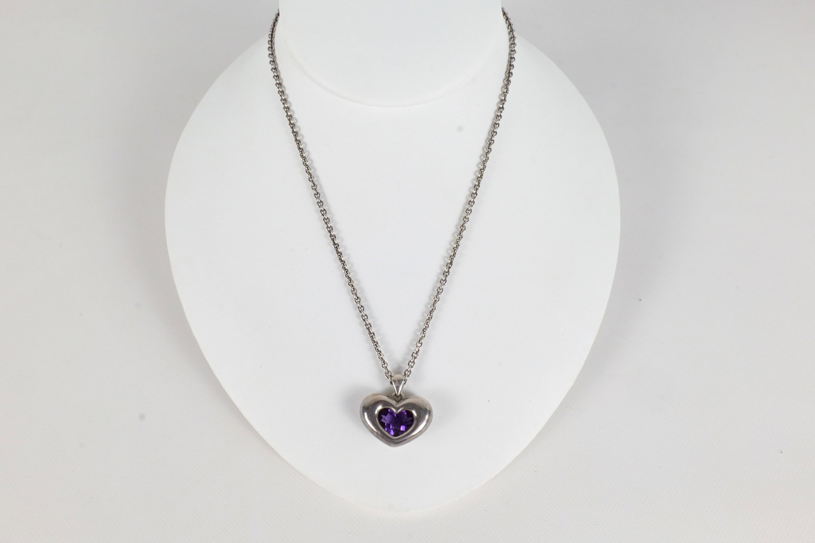 Movado Sterling and 18K Necklace: A Movado sterling and 18 K amethyst necklace. The necklace is sterling silver with an 18 K Movado emblem in the links, and the pendant is a sterling heart pendant with an amethyst in this center and a