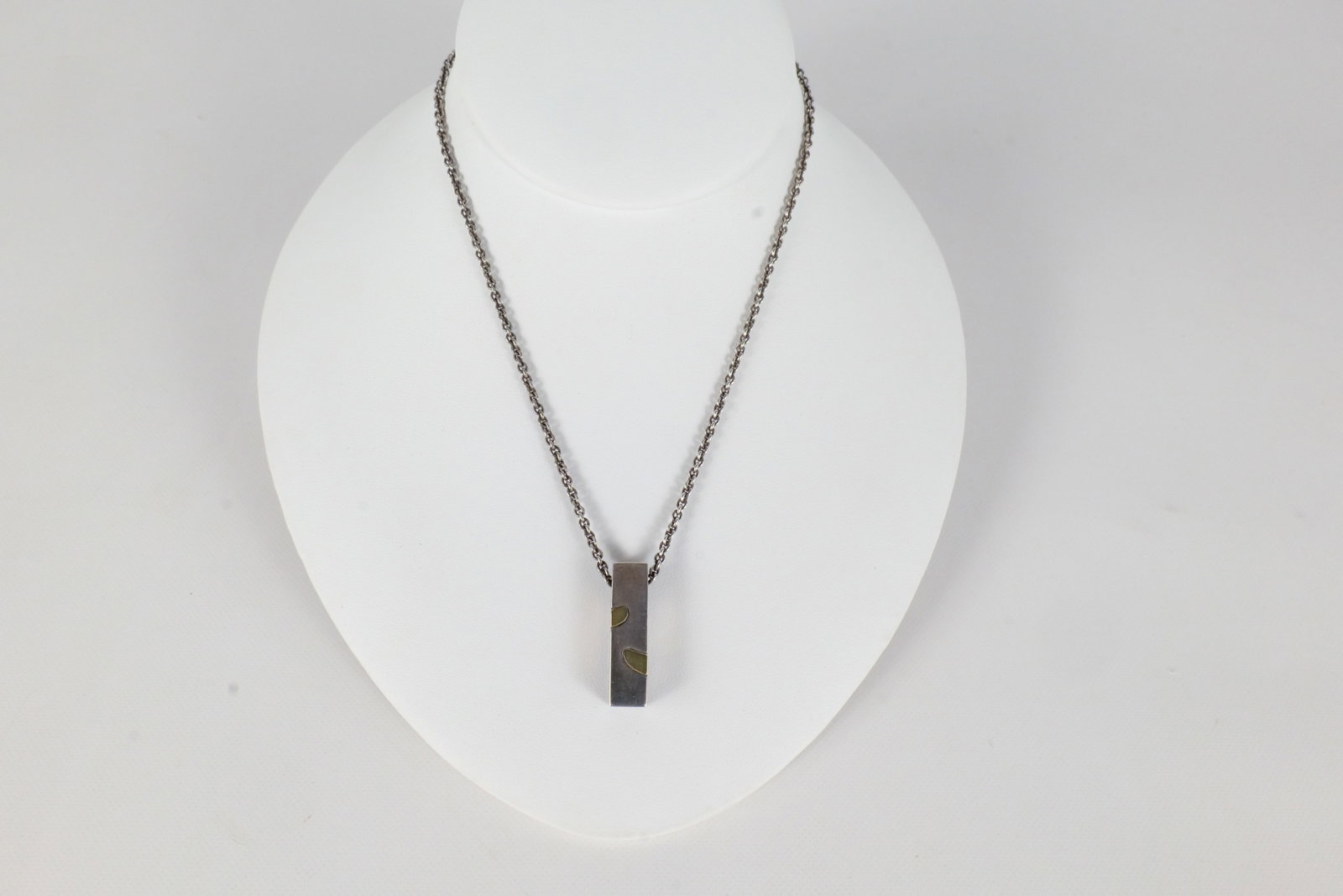 Movado Sterling and 18K Necklace: A Movado sterling silver and 18 K gold necklace. The necklace features an 18 K logo emblem within the links and the rectangular modernist drop pendant features 18 K inlaid modern spots with an 18 K Mo