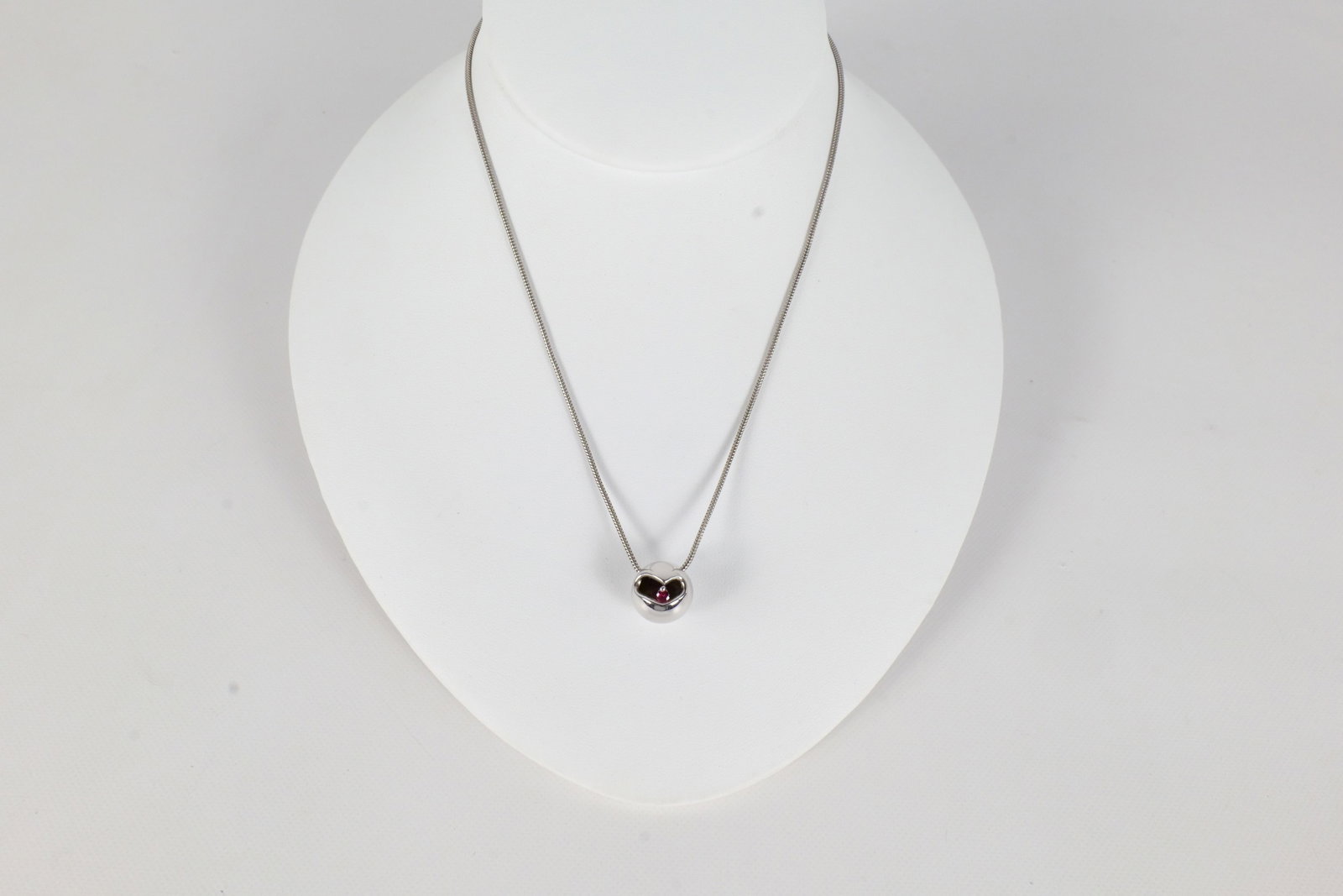 Movado Sterling Necklace: A Movado sterling silver necklace with a sterling chain a circular pendant with a cut out in the center and a small red stone. The chain measures approximately 15". All invoices must be paid within 24