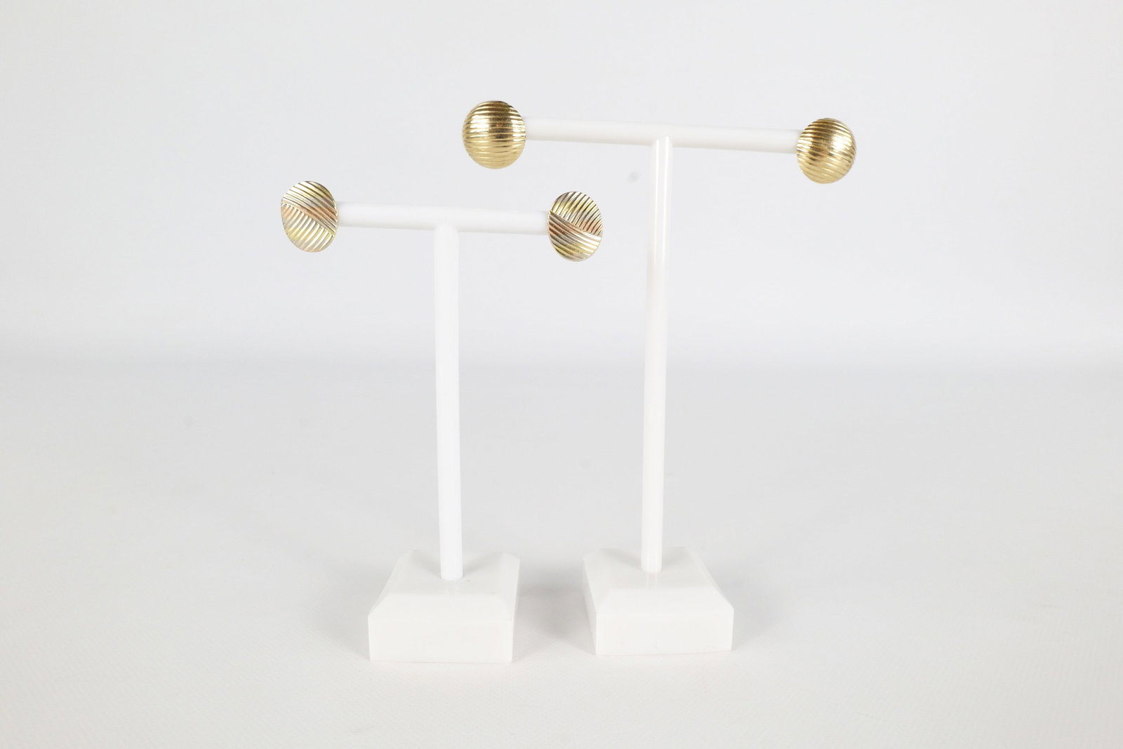 2 Pairs 14K Earrings: Two pairs of 14 K earrings. The first pair is an Oval shape with Criss crossing lines in a slight Tri color gold along the front and is marked on the post. The second pair is a circular earring with