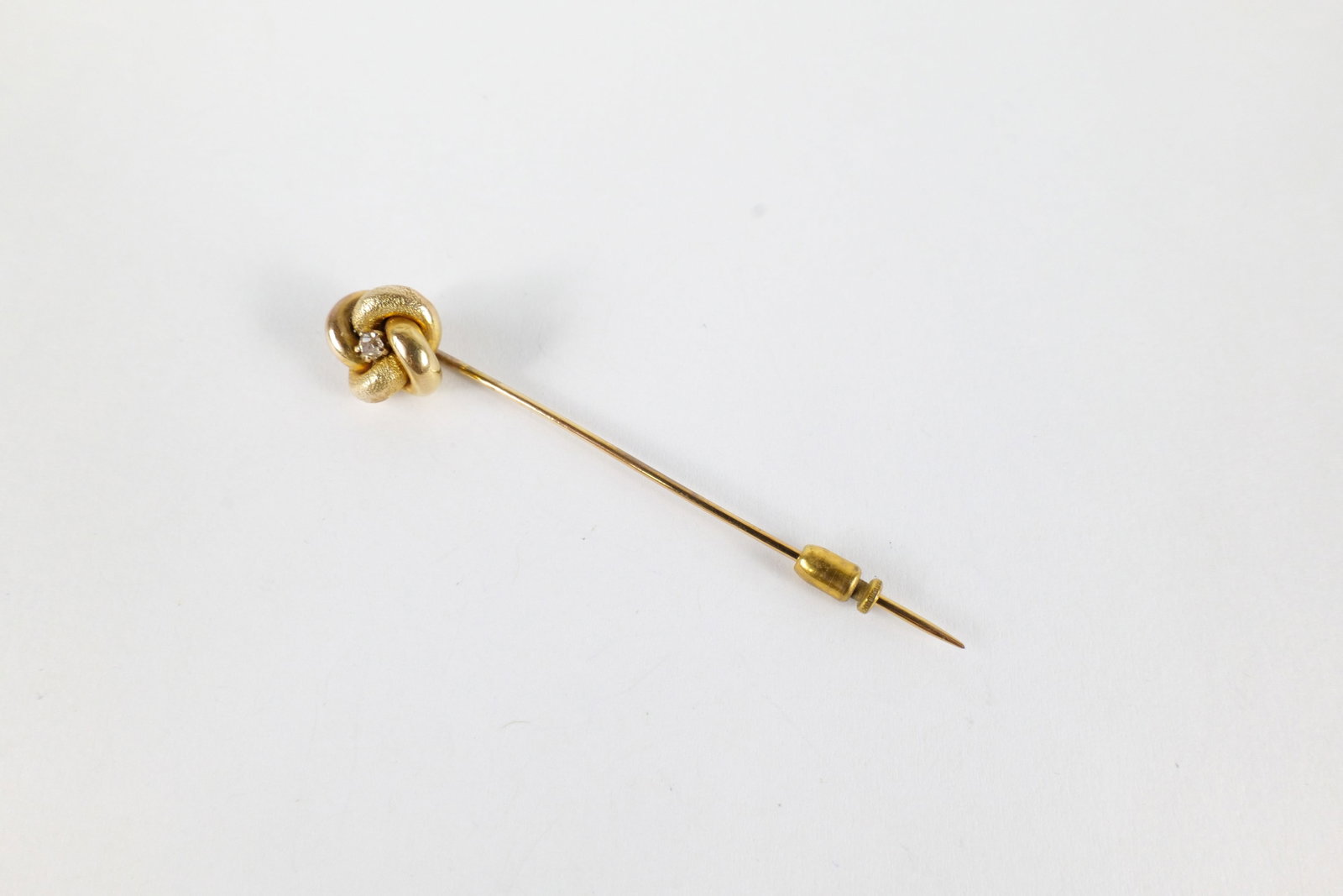 10K & Diamond Stick Pin: 10 K yellow gold and diamond stick pin. Has a knot style head in shiny and buffed gold with a small round cut diamond in the center. Both the head and the stick are 10 K. Was tested is not marked. Mea