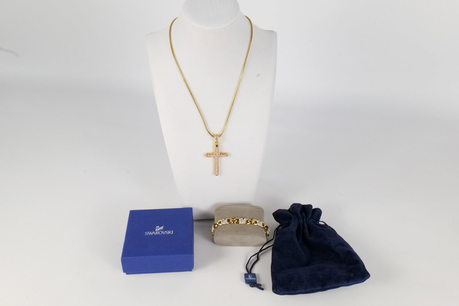 Lot of Costume Jewelry: Gold Tone Swarovski Cross Pendant Necklace and More. The lot includes an adjustable 17” long gold tone snake chain with a gold tone cross pendant studded with light pink crystal rhinestones by S