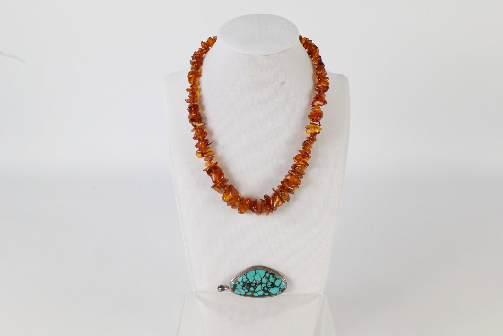 Lot of Sterling and Amber Jewelry: A lot of jewelry including a sterling silver pendant with a pressed turquoise center and an amber necklace with graduated amber beads of different shapes. The necklace measures approximately 17" and t