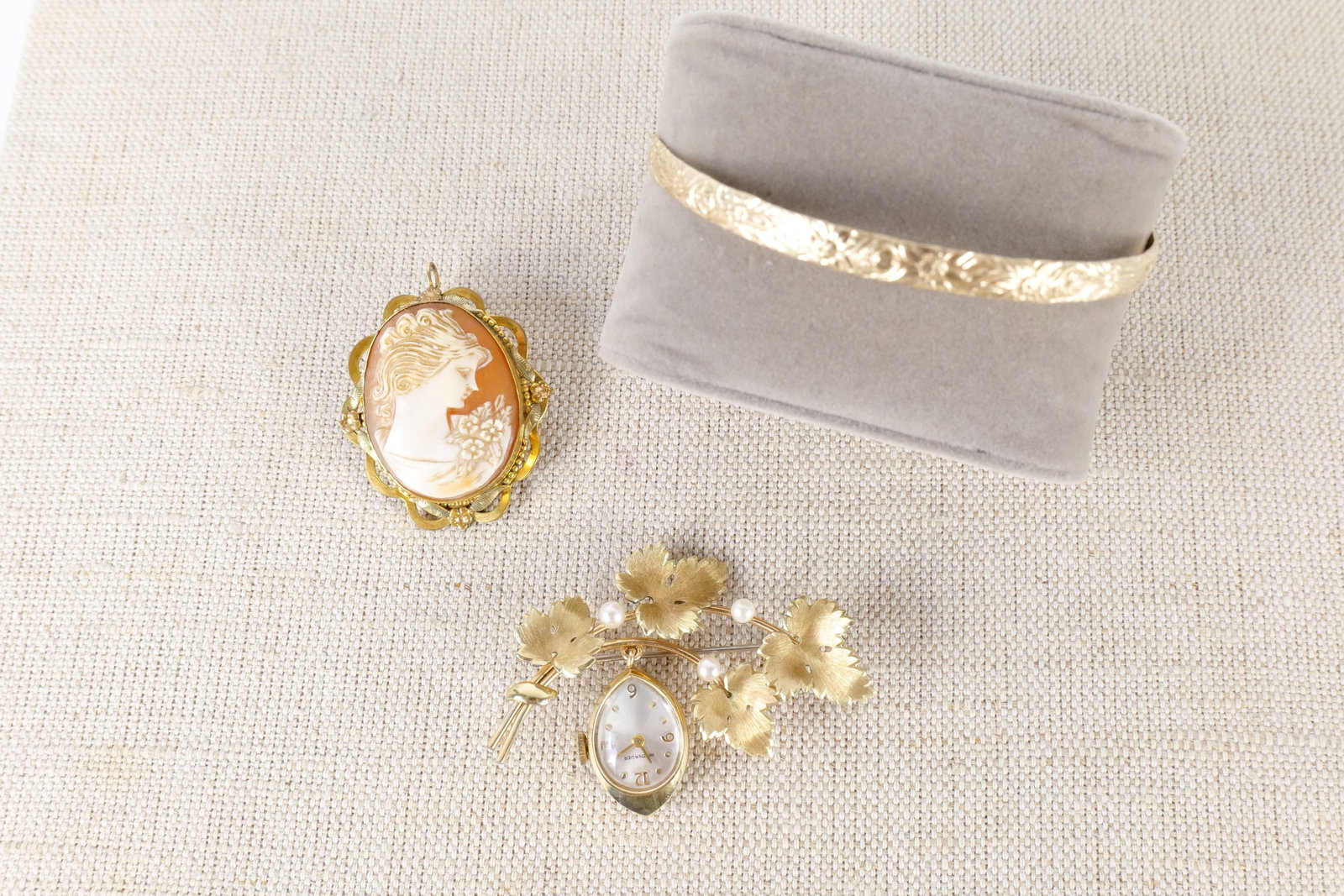 Lot of Gold Filled Jewelry: Lot of gold filled jewelry including a cameo with a gold filled frame, a bangle bracelet with floral etching on the front, and a watch pin by Witnauer with leaves and seed pearls. All invoices must be