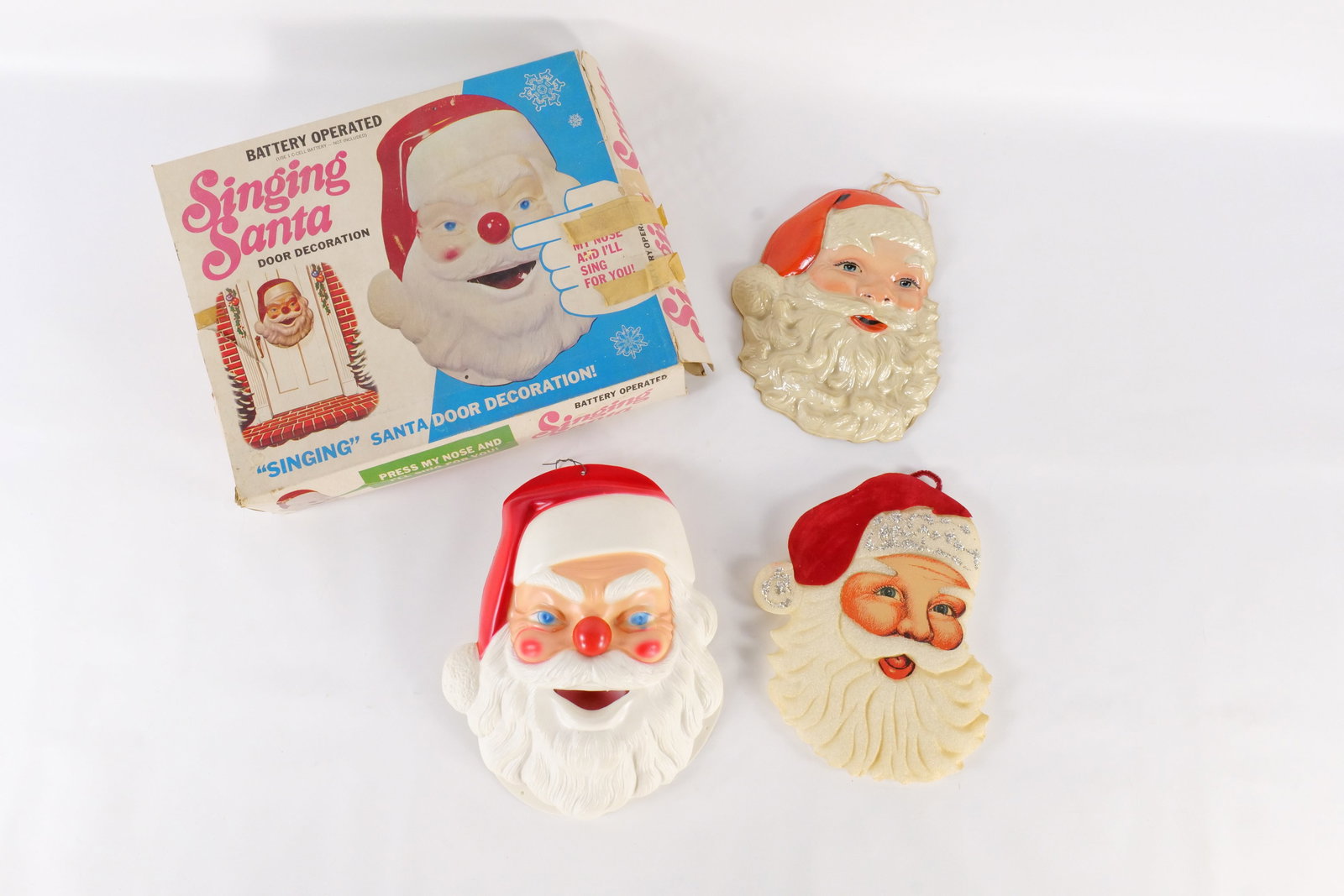 Lot of Santa Head Decorations: Lot of Santa Head Decorations. Including Battery Operated Singing Santa Door Decoration with Box - Missing Door to Battery Case, 2 Plastic Santa Heads, and Styrofoam Head. One has a chip to beard. Box