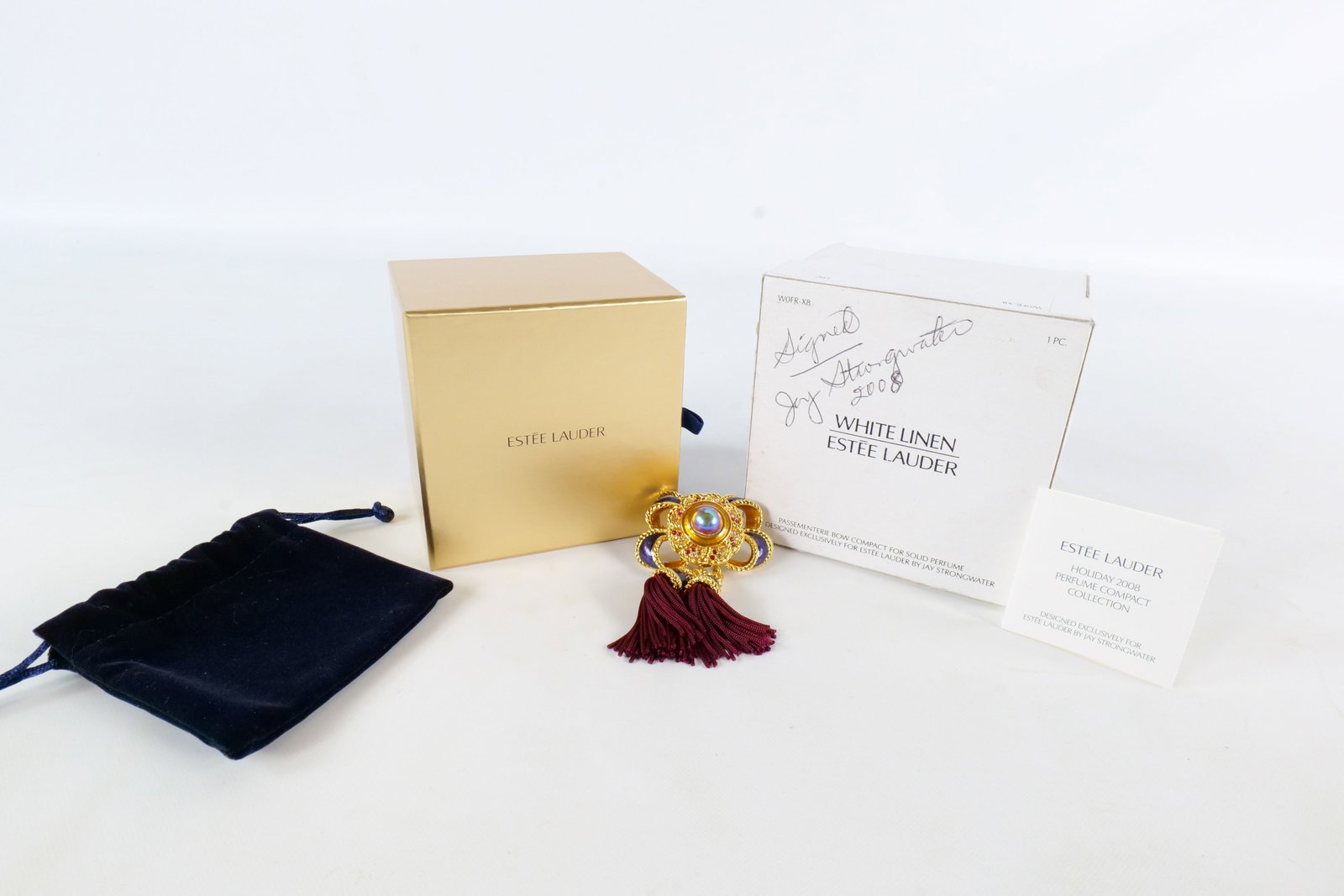 Estee Lauder/Jay Strongwater Passementerie Bow Perume Compact - Signed: 2008 Estee Lauder Passementerie Bow compact for solid perfume - White Linen. Designed by Jay Strongwater. Unused. Gold tone bow with blue enamel accents and a large cabochon opalescent stone and small