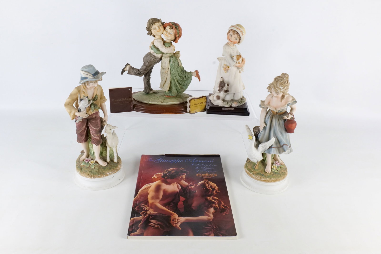 Group of Figurines: Group of figurines including Armani Embracing Boy and Girl (has flake on her hat), Armani Girl with Cat and Puppy (cat missing ear), Armani magazines and catalogs and a pair of Japanese bisque figurin
