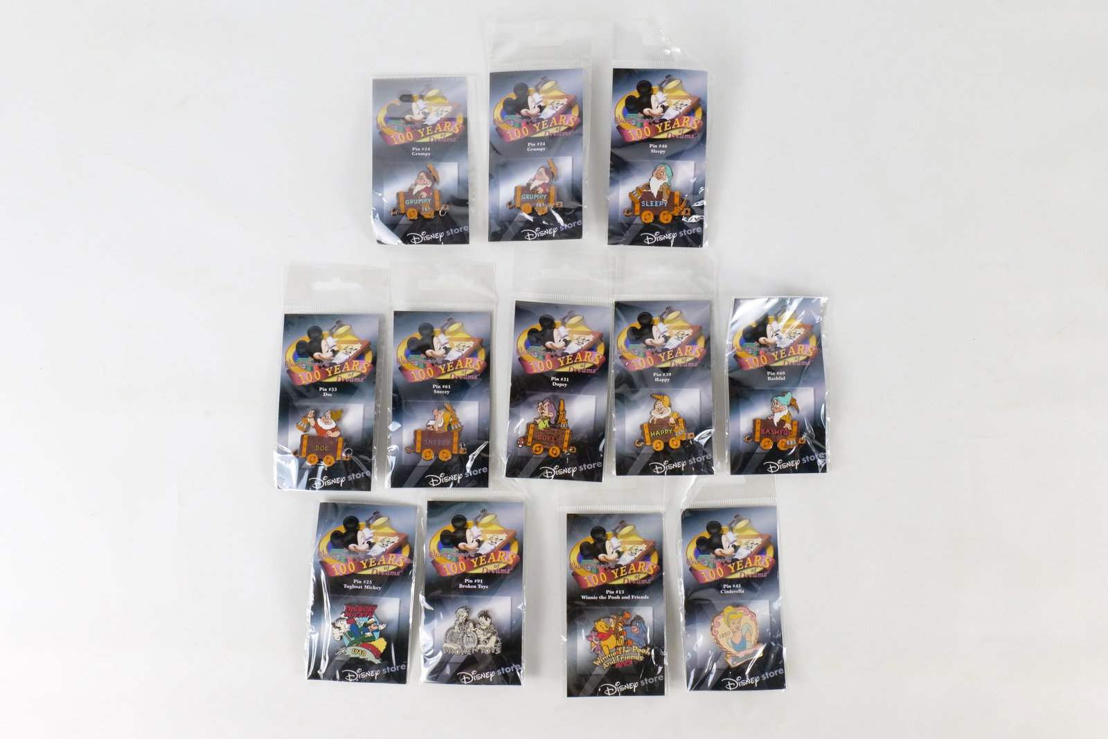 Lot of 12 Sealed 100 Years of Dreams Pins: Lot of 12 Sealed 100 Years of Dreams Pins. Including All Seven Dwarfs in Mine Carts with an Extra Grumpy, Broken Toys, Cinderella, Tugboat Mickey, and Winnie the Pooh and Friends. All invoices must be