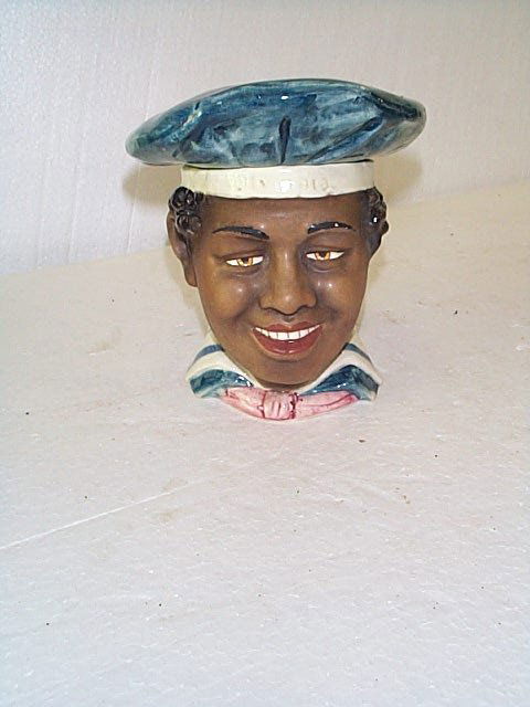 Porcelain figural tobacco jar head depicting a bla: Porcelain figural tobacco jar head depicting a black man with a head band entitled Olympia. Measures 6.25" tall. Buyer to pay $20.00 shipping and handling, all items to be sent USPS Priority Mail with