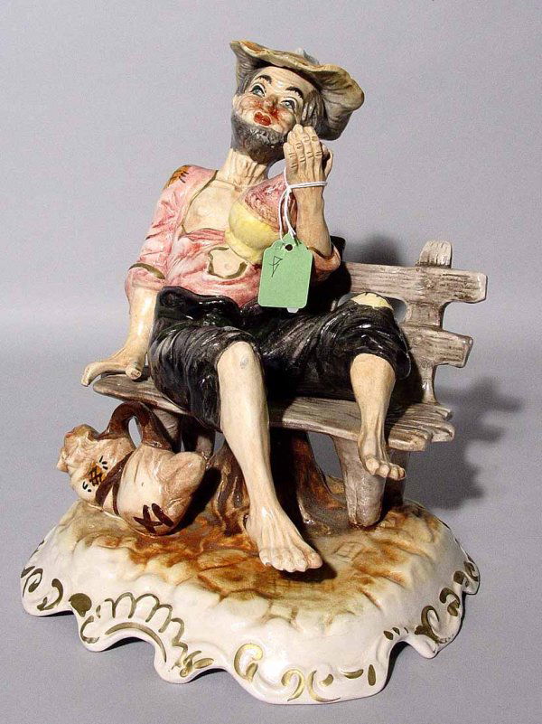AMUSING CAPO DE MONTE FIGURE, depicting a man sit: AMUSING CAPO DE MONTE FIGURE, depicting a man sitting on a park bench holding a wine bottle; 11 inch height (Est. 30-45)