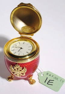 GILT METAL AND ENAMEL EGG FORM CLOCK ON STAND: GILT METAL AND ENAMEL EGG FORM CLOCK ON STAND, having a quartz movement and hinged lid; 3 inch height (Est. 40-60)