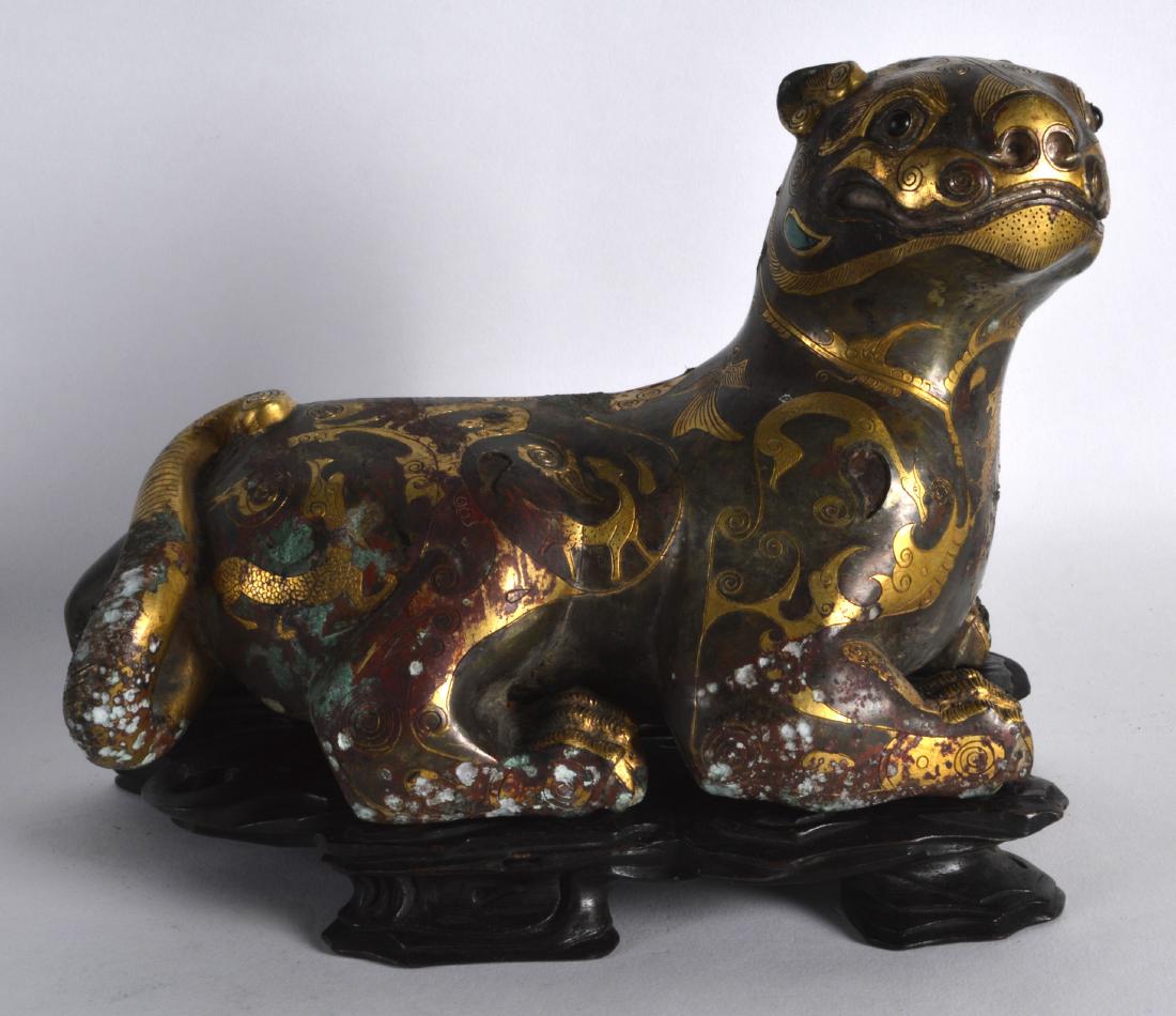 A LOVELY CHINESE GILT BRONZE FIGURE OF A BUDDHISTIC: A LOVELY CHINESE GILT BRONZE FIGURE OF A BUDDHISTIC BEAST modelled upon a fitted hardwood base, decorated with animals, motifs and foliage. 7.5ins wide.