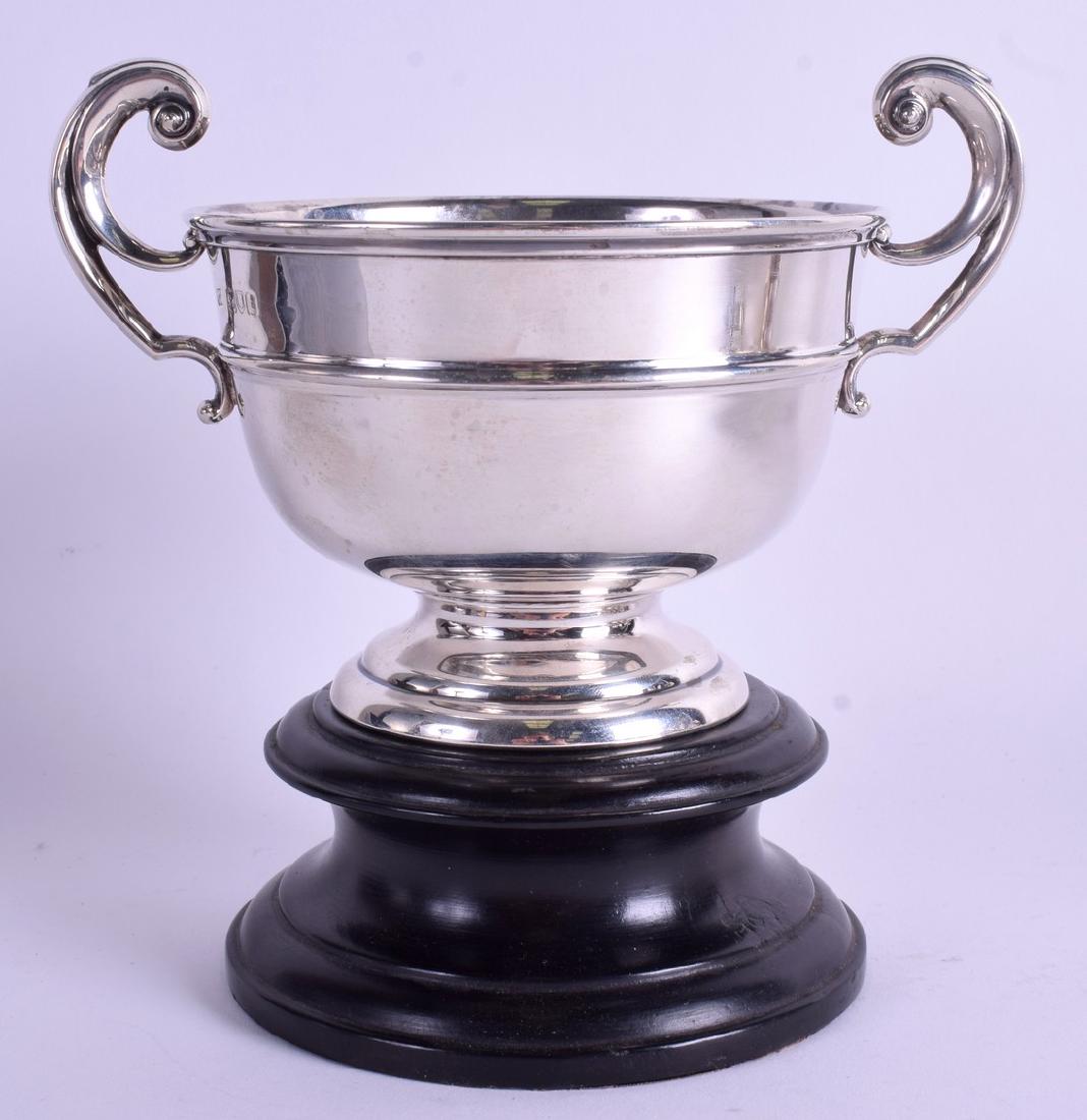 A SOLID SILVER TROPHY BY MAPPIN & WEBB, formed with: A SOLID SILVER TROPHY BY MAPPIN & WEBB, formed with twin handles upon a wooden stand. 17 cm wide & weight 7.5 oz.
