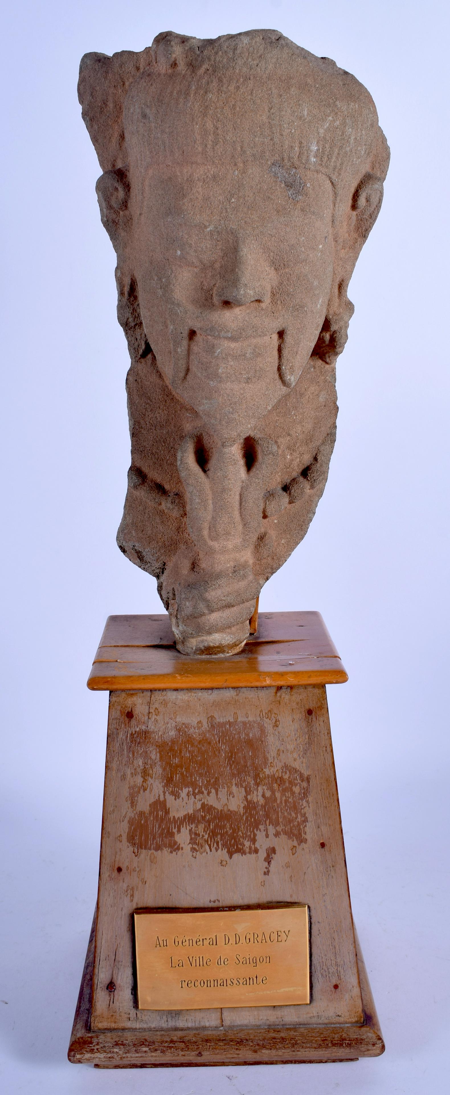 AN EARLY CAMBODIAN CARVED SANDSTONE BUST OF A BEARDED: AN EARLY CAMBODIAN CARVED SANDSTONE BUST OF A BEARDED MALE modelled upon a wooden plinth. Head 24 cm x 9 cm.