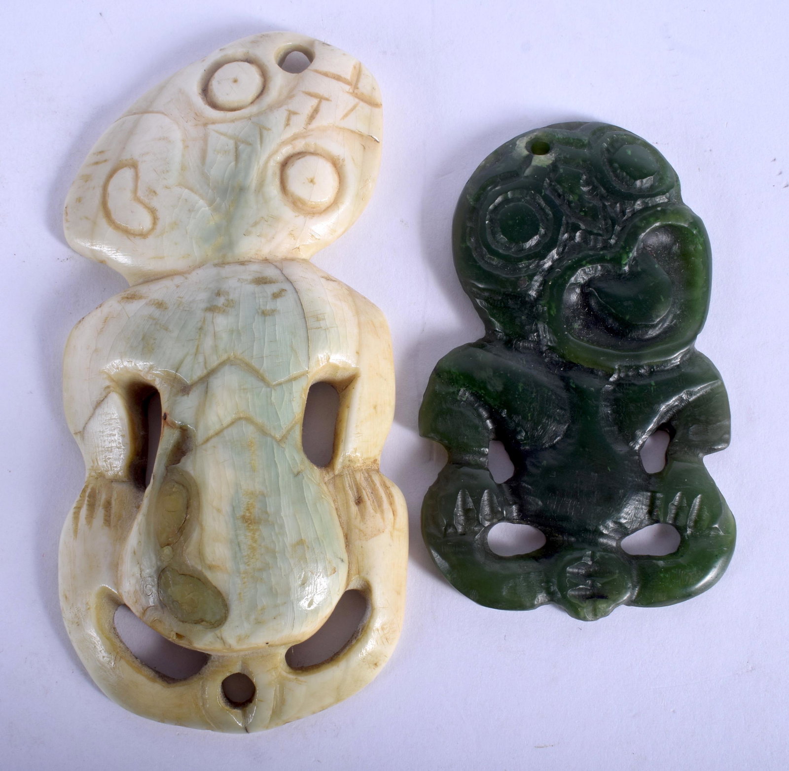 A MAORI TRIBAL NEPHRITE CARVED NECK PENDANT Hei Tiki,: A MAORI TRIBAL NEPHRITE CARVED NECK PENDANT Hei Tiki, New Zealand, together with a similar horn Hei Tiki pendant. 4.5 cm x 6.5 cm & 5 cm x 10 cm. (2)