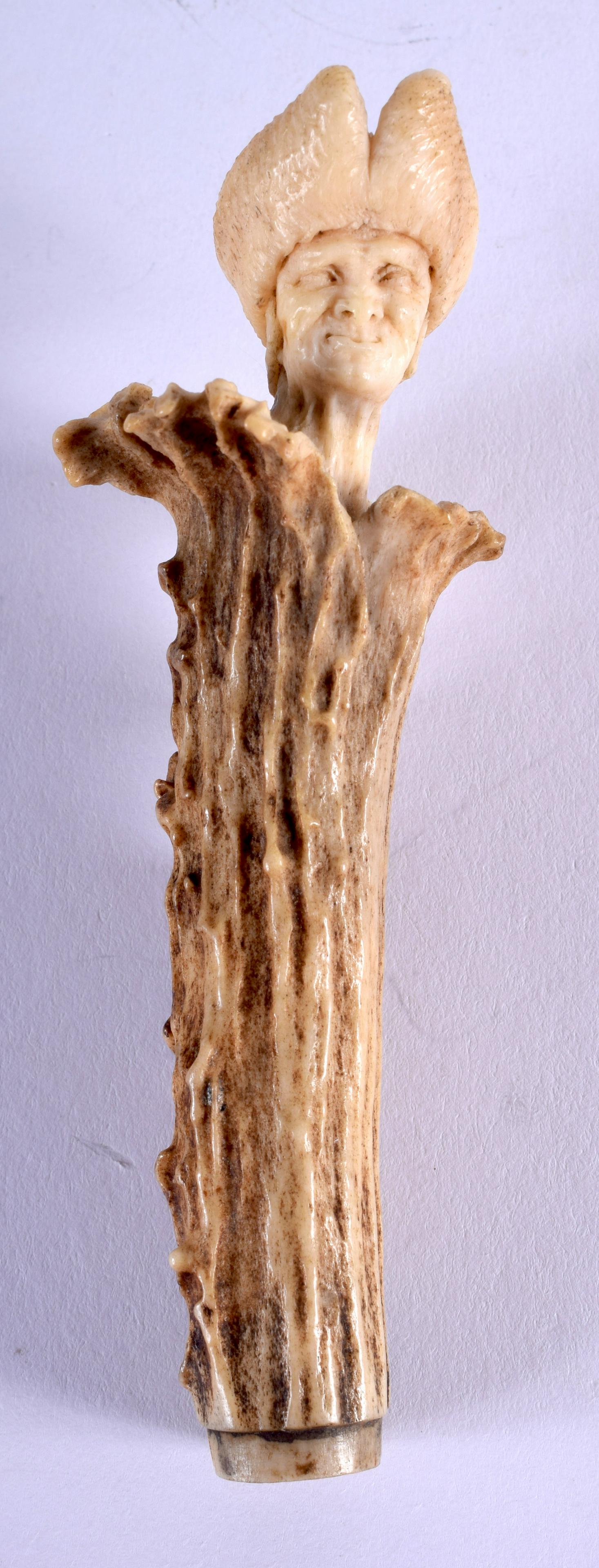 A 19TH CENTURY BAVARIAN BLACK FOREST CARVED STAG ANTLER: A 19TH CENTURY BAVARIAN BLACK FOREST CARVED STAG ANTLER HANDLE formed as a male wearing a hat. 10.25 cm long.