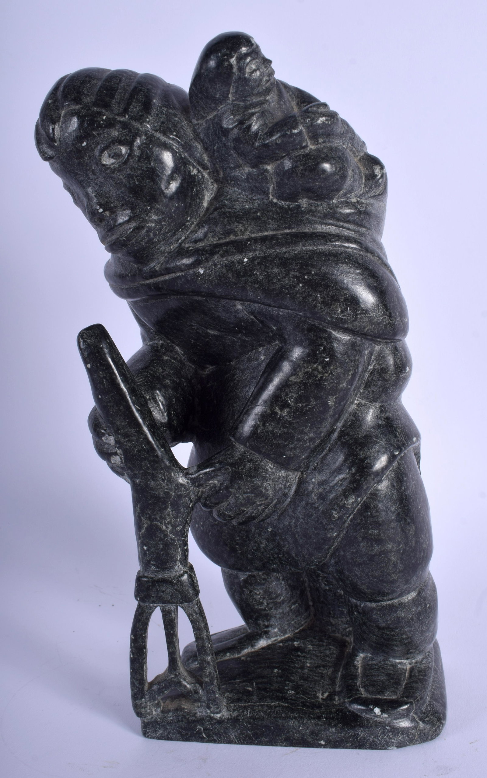 A NORTH AMERICAN CARVED INUIT SOAPSTONE FIGURE OF A: A NORTH AMERICAN CARVED INUIT SOAPSTONE FIGURE OF A HUNTER modelled with a child upon there back. 27 cm x 10 cm.