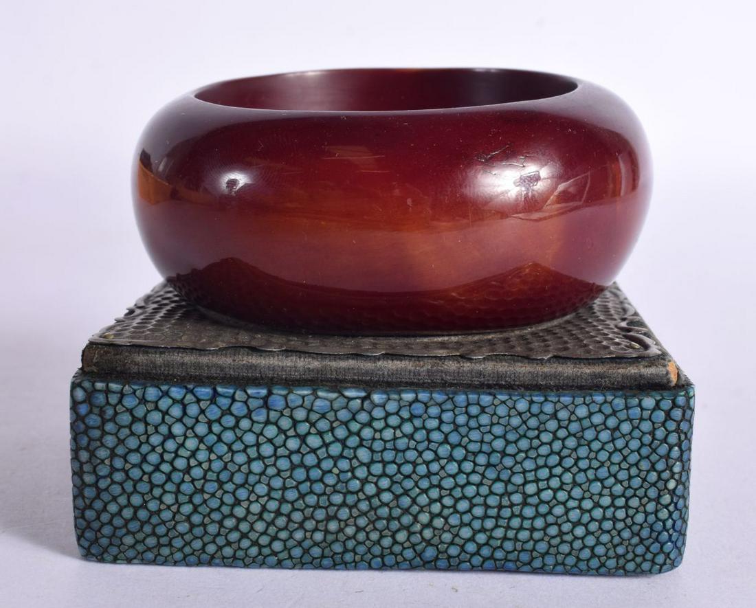 A CHERRY AMBER TYPE BANGLE upon a shagreen stand. 7.5 cm diameter.: A CHERRY AMBER TYPE BANGLE upon a shagreen stand. 7.5 cm diameter.