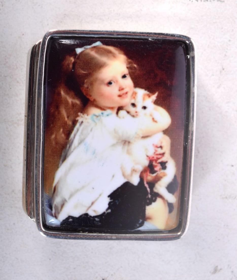 A SILVER AND ENAMEL PILL BOX WITH THE LID DECORATED WITH A YOUNG GIRL HOLDING HER CAT. Stamped Ster: A SILVER AND ENAMEL PILL BOX WITH THE LID DECORATED WITH A YOUNG GIRL HOLDING HER CAT. Stamped Sterling, 3.2cm x 2.6cm x 1.3cm, weight 19.3g