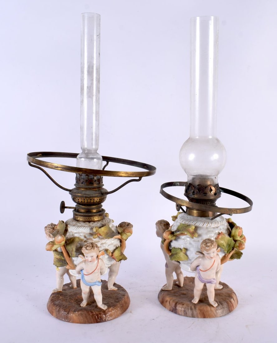 A PAIR OF ANTIQUE GERMAN PORCELAIN OIL LAMPS formed with putti holding aloft floral encrusted bodies (1 of 4)