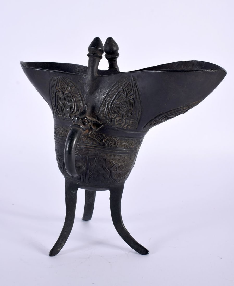 A CHINESE QING DYNASTY BRONZE JUE WINE VESSEL decorated with archaic motifs and emblems. 18cm x 15cm: A CHINESE QING DYNASTY BRONZE JUE WINE VESSEL decorated with archaic motifs and emblems. 18cm x 15cm.