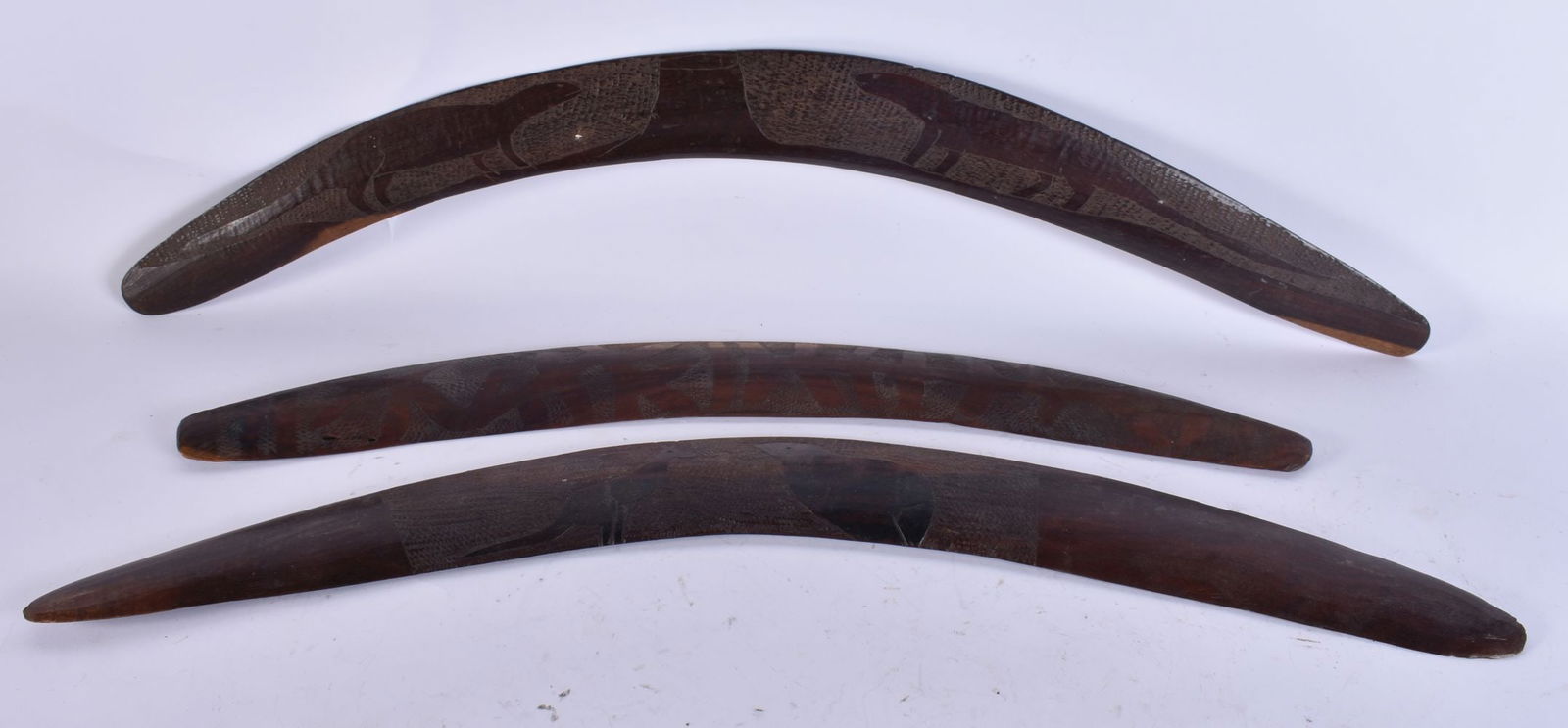 THREE AUSTRALIAN TRIBAL ABORIGINAL CARVED WOOD BOOMERANGS two decorated with animals and motifs. Lar: THREE AUSTRALIAN TRIBAL ABORIGINAL CARVED WOOD BOOMERANGS two decorated with animals and motifs. Largest 68 cm wide. (3)