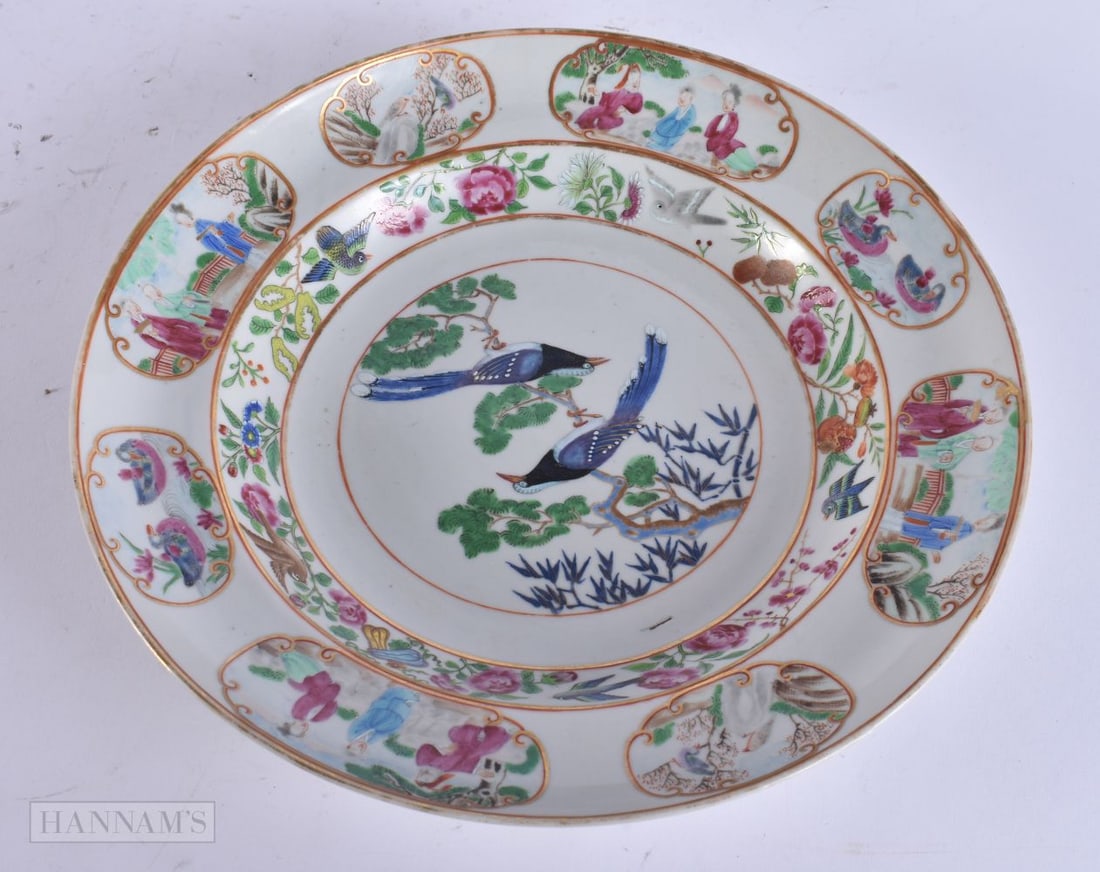 A FINE AND RARE 19TH CENTURY CHINESE CANTON FAMILLE ROSE PLATE painted with two birds within panels: A FINE AND RARE 19TH CENTURY CHINESE CANTON FAMILLE ROSE PLATE painted with two birds within panels of figures and landscapes. 24 cm diameter.