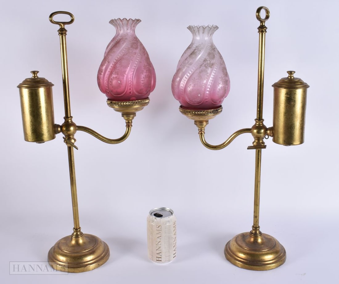 A PAIR OF ANTIQUE BRASS COLZA LAMPS with cranberry shades. 58cm high.: A PAIR OF ANTIQUE BRASS COLZA LAMPS with cranberry shades. 58cm high.