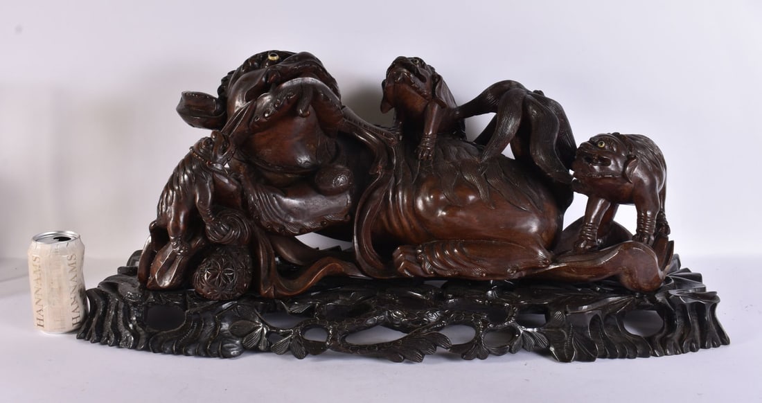 A LARGE 19TH CENTURY CHINESE CARVED HARDWOOD MODEL OF A RECUMBENT BUDDHISTIC LION WITH CUBS ON STAND: A LARGE 19TH CENTURY CHINESE CARVED HARDWOOD MODEL OF A RECUMBENT BUDDHISTIC LION WITH CUBS ON STAND naturalistically carved with a brocade ball and ribbon, the lion and cubs with inlaid eyes, set on 