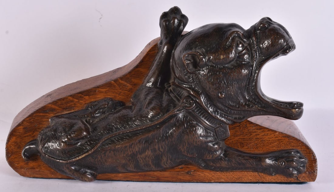 A LATE 19TH CENTURY BOOTJACK MODELLED AS A BRONZE BULLDOG AN ON OAK BASE in relief as a recumbent bu: A LATE 19TH CENTURY BOOTJACK MODELLED AS A BRONZE BULLDOG AN ON OAK BASE in relief as a recumbent bulldog with open mouth and raised forepaw wearing a studded collar, the collar signed 1888. 35 cm wid