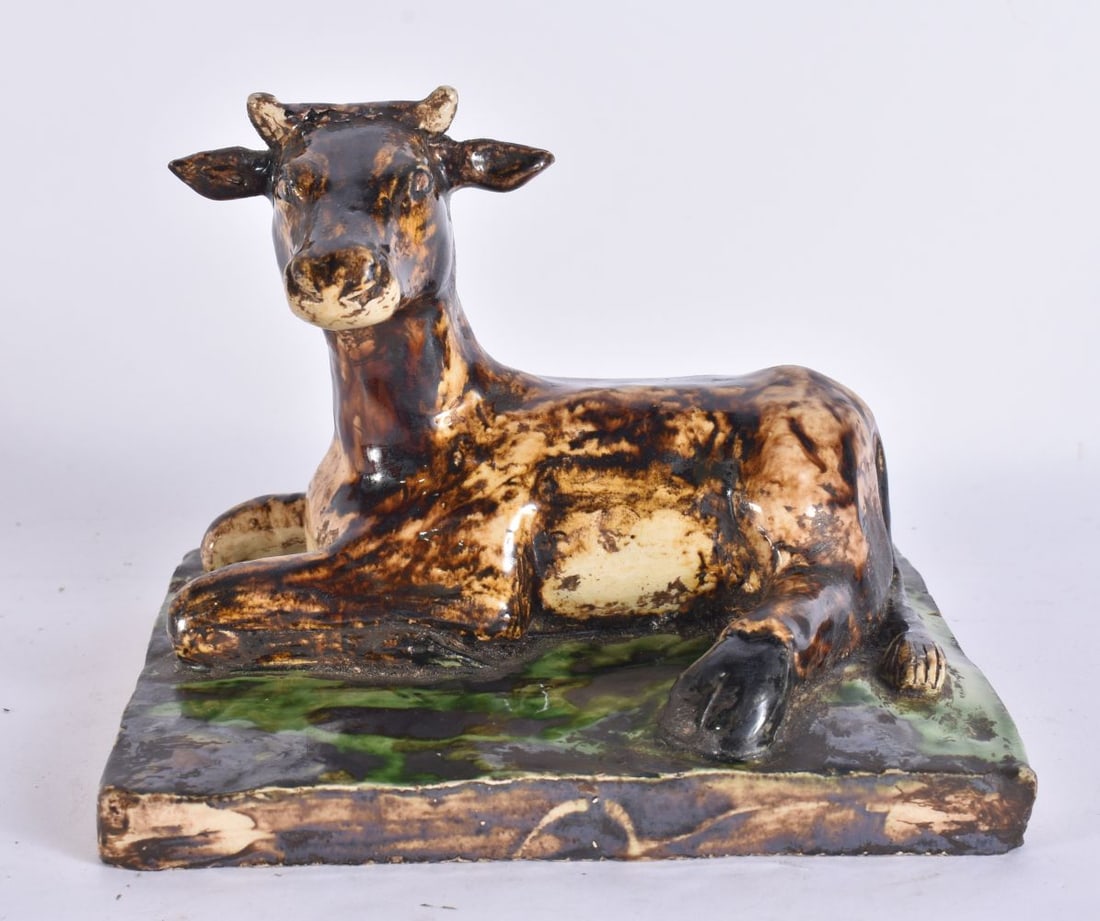 AN EARLY 19TH CENTURY CONTINENTAL POTTERY FIGURE OF A COW modelled upon a square form base. 15 cm x (1 of 6)