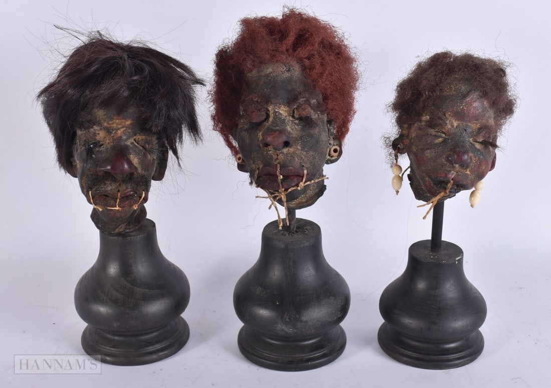THREE SOUTH AMERICAN TRIBAL HEADS upon later ebonised wood stands. 25 cm high. (3) (1 of 7)