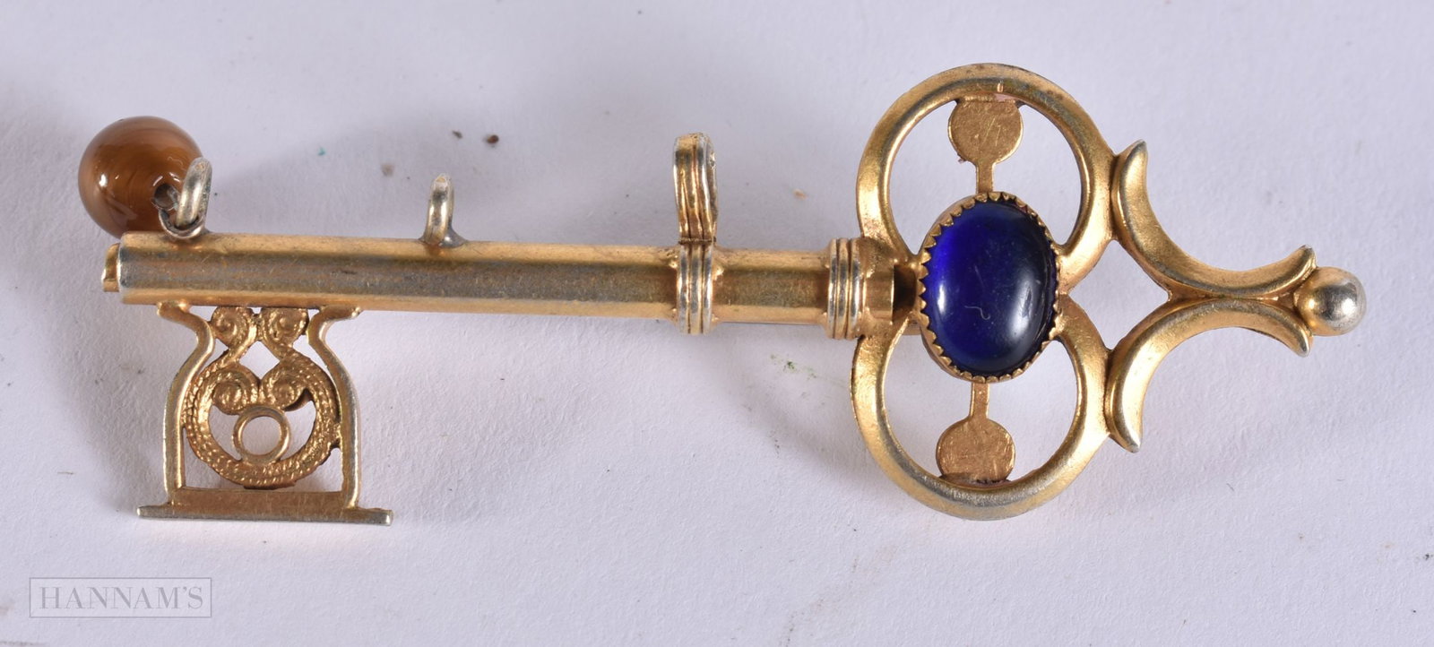 AN ANTIQUE YELLOW METAL KEY BROOCH inset with turquoise, sapphire and tigers eye. 7.7 grams. 7 cm wi: AN ANTIQUE YELLOW METAL KEY BROOCH inset with turquoise, sapphire and tigers eye. 7.7 grams. 7 cm wide.