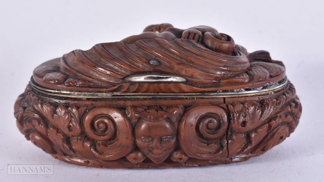 A FINE EARLY 18TH CENTURY FRENCH COQUILLA NUT SNUFF BOX carved with a putti upon a shell holding a t: A FINE EARLY 18TH CENTURY FRENCH COQUILLA NUT SNUFF BOX carved with a putti upon a shell holding a trident. 7.5 cm x 3.5 cm.