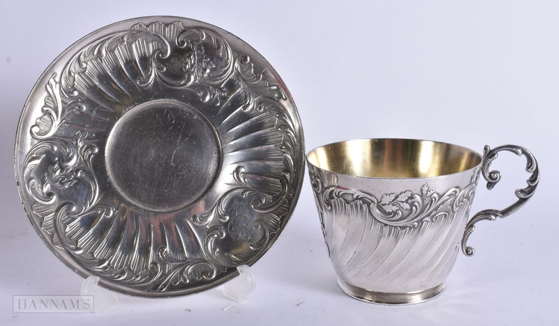 AN ART NOUVEAU WHITE METAL BREAKFAST CUP AND SAUCER. Largest 17 cm wide. (2): AN ART NOUVEAU WHITE METAL BREAKFAST CUP AND SAUCER. Largest 17 cm wide. (2)