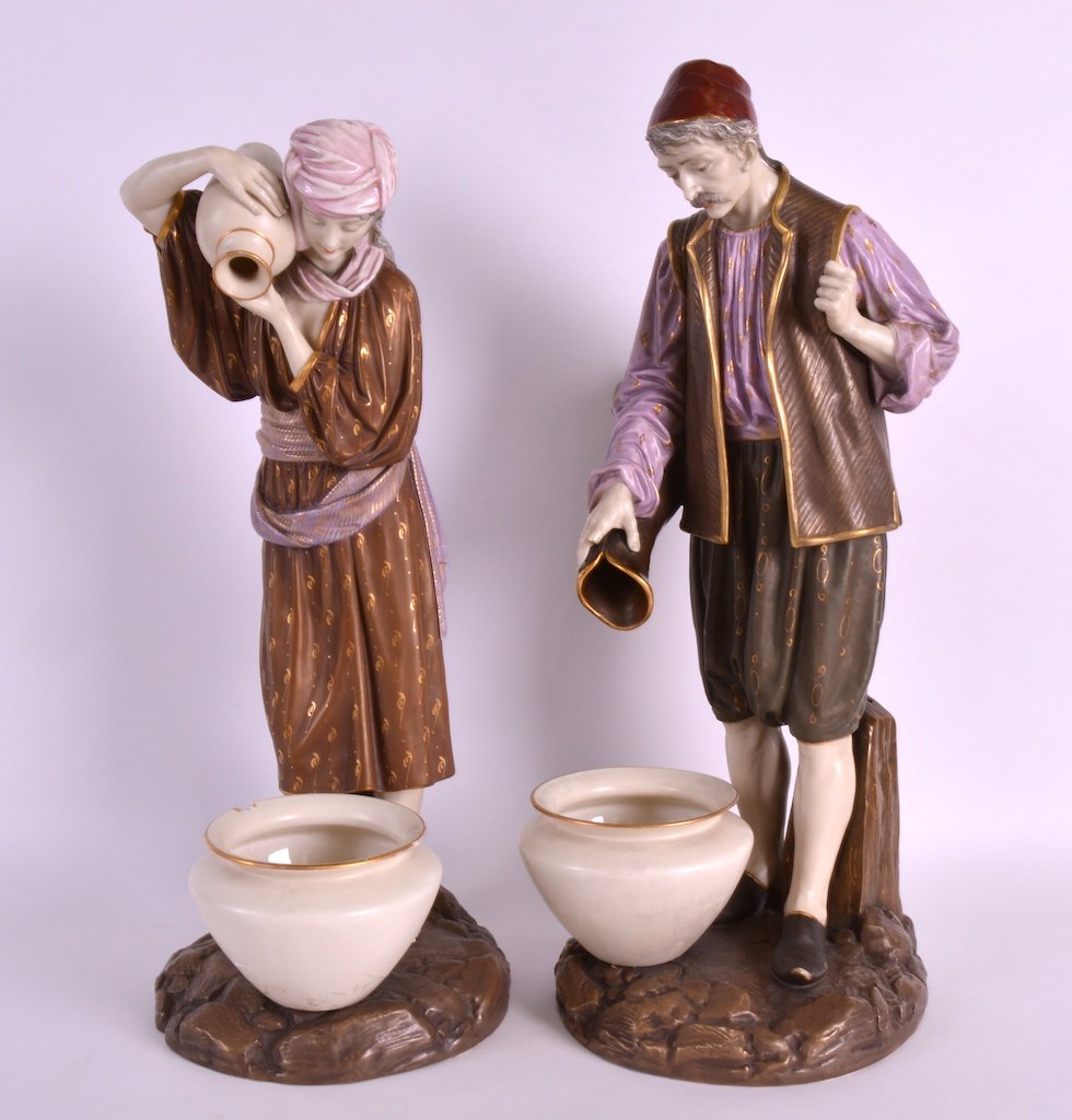 A PAIR OF LATE 19TH CENTURY ROYAL WORCESTER FIGURES OF: A PAIR OF LATE 19TH CENTURY ROYAL WORCESTER FIGURES OF MIDDLE EASTERN WATER CARRIERS modelled pouring a ewer into an urn, upon raised rocky bases. 1ft 4.5ins high.
