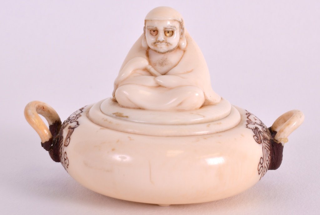 A 19TH CENTURY JAPANESE MEIJI PERIOD IVORY BOX AND: A 19TH CENTURY JAPANESE MEIJI PERIOD IVORY BOX AND COVER formed as a seated daruma, the body carved with beasts. Signed. 2.5ins wide. £80-120