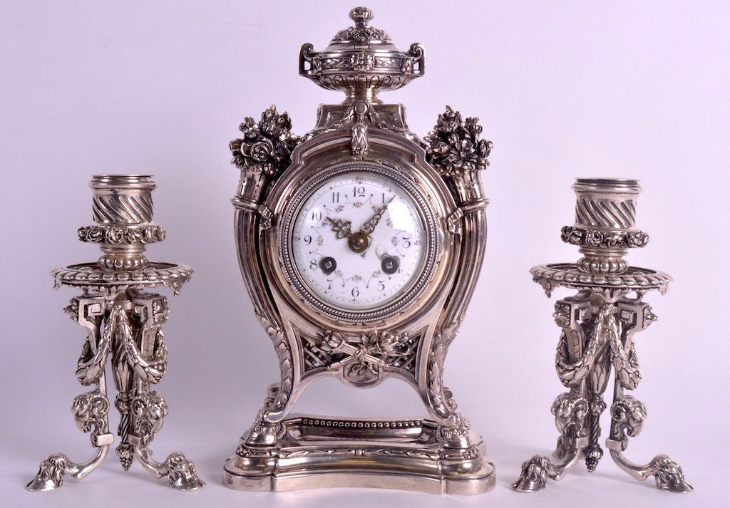 A FINE 19TH CENTURY FRENCH SILVER CLOCK GARNITURE Paris: A FINE 19TH CENTURY FRENCH SILVER CLOCK GARNITURE Paris C1890, by Alphonse Debain, comprising of mantel clock with scrolling foliate dial, supported upon hoof feet, together with matching candlesticks