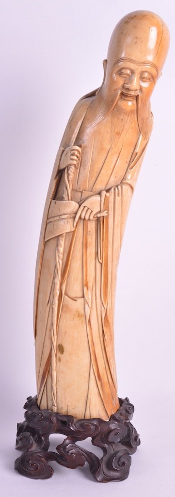 A 17TH CENTURY CHINESE CARVED IVORY FIGURE OF AN: A 17TH CENTURY CHINESE CARVED IVORY FIGURE OF AN IMMORTAL Ming Dynasty, modelled with one hand inside his long robe, supported on a fitted hardwood base. 13ins high. Provenance: Private Swiss Collecti