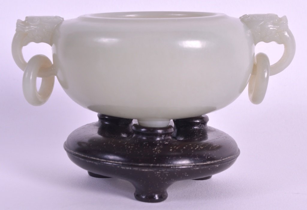 A GOOD 18TH CENTURY CHINESE CARVED WHITE JADE TWIN: A GOOD 18TH CENTURY CHINESE CARVED WHITE JADE TWIN HANDLED VESSEL with buddhistic lion mask head handles, upon a fitted hardwood base. Jade 4.5ins wide. Provenance: Purchased in Peking C1950, Private