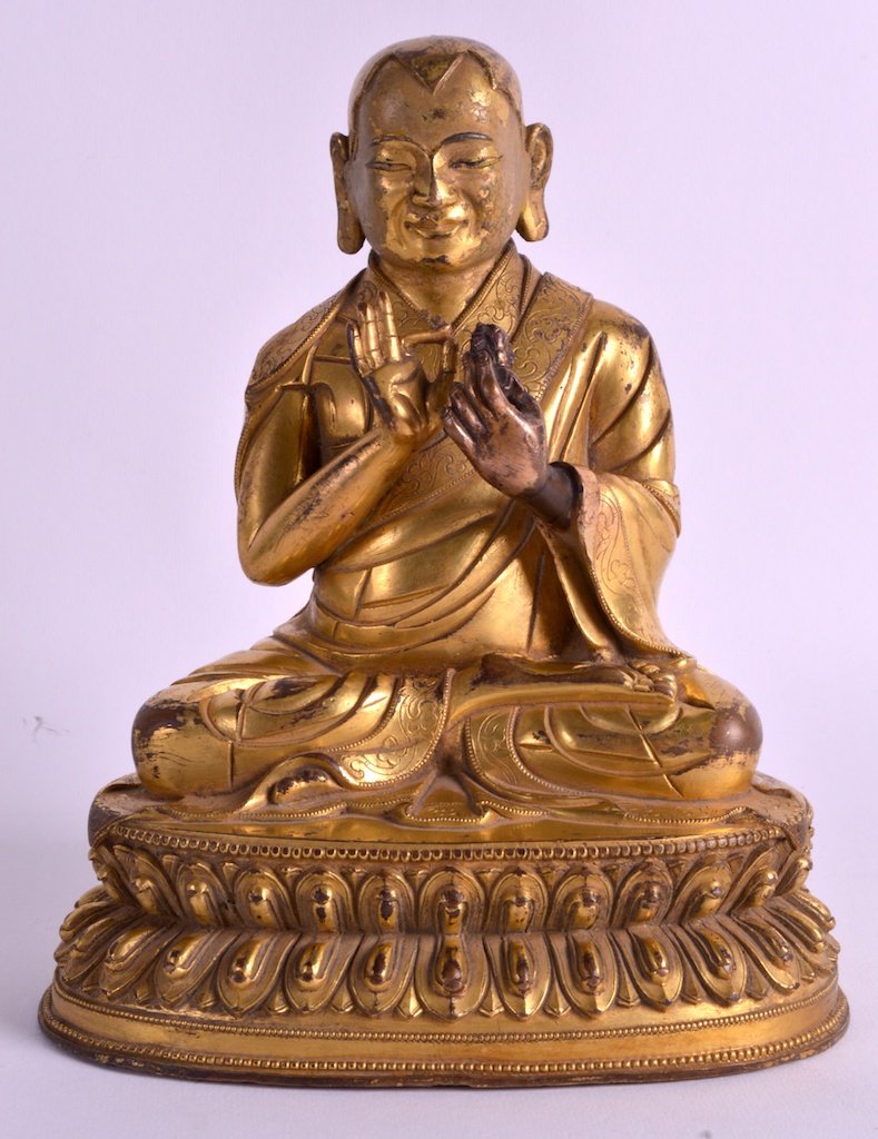 A CHINESE QING DYNASTY GILT BRONZE FIGURE OF A: A CHINESE QING DYNASTY GILT BRONZE FIGURE OF A BUDDHISTIC LAMA probably C1800, modelled with one hand raised, wearing foliate embellished robes, upon a triangular capped lotus base. 7.5ins high.