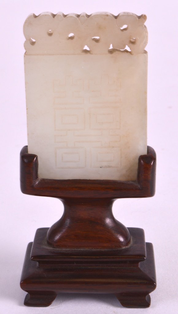 A 19TH CENTURY CHINESE CARVED GREEN JADE PLAQUE Qing,: A 19TH CENTURY CHINESE CARVED GREEN JADE PLAQUE Qing, decorated with Shou characters, upon a hardwood base. Jade 2ins x 1.25ins.