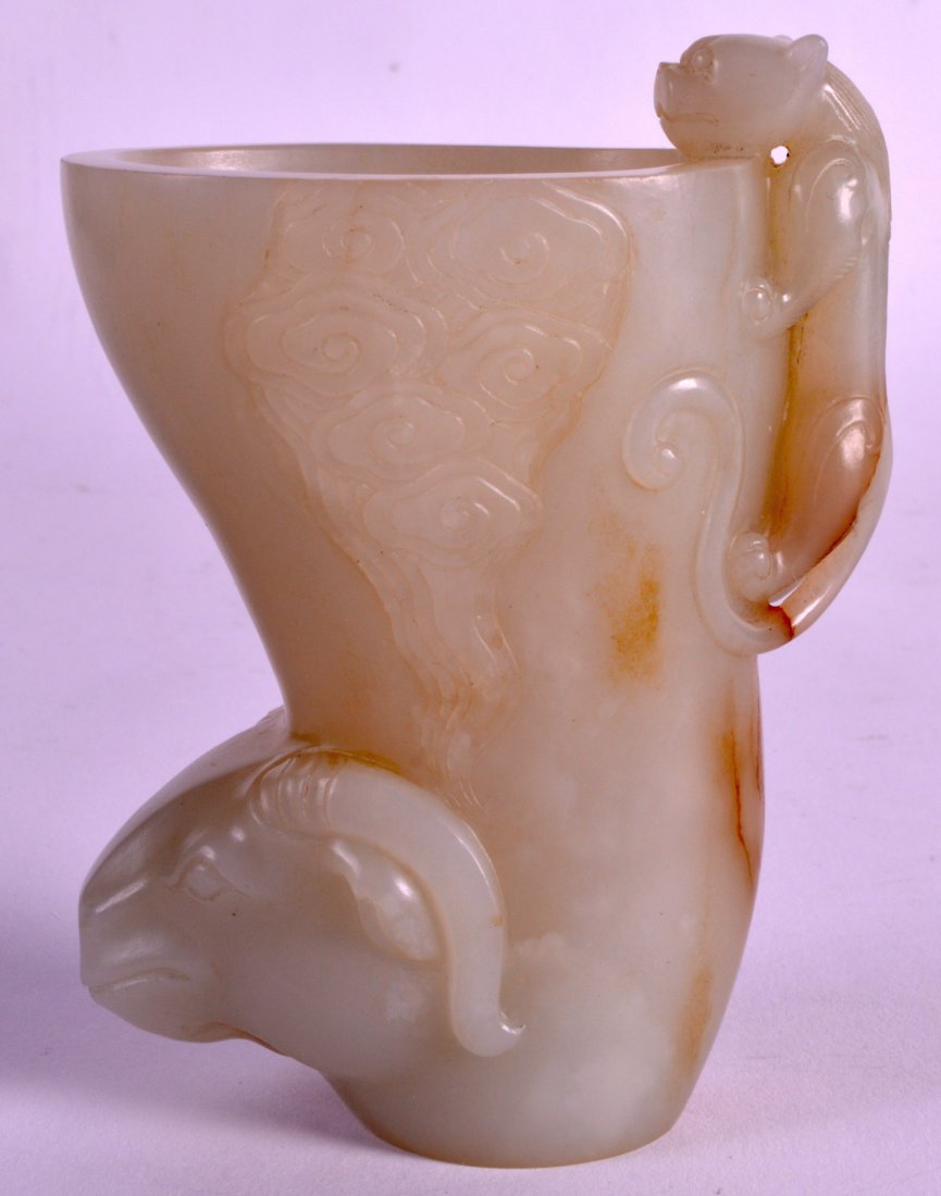 A CHINESE QING DYNASTY CARVED PALE GREEN JADE LIBATION: A CHINESE QING DYNASTY CARVED PALE GREEN JADE LIBATION CUP modelled as a rams head with clambering chilong. 4Ins high.