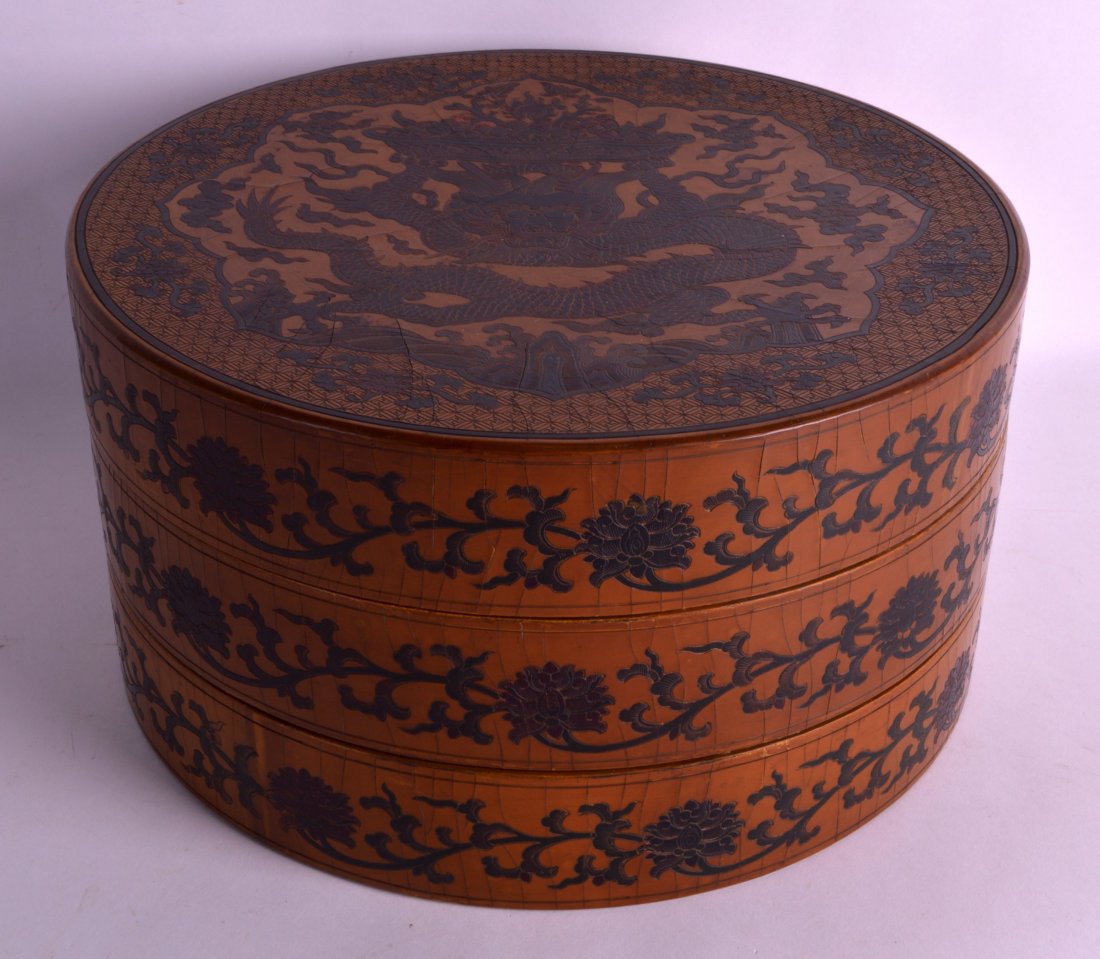A CHINESE BROWN LACQUER THREE TIER CIRCULAR BOX AND: A CHINESE BROWN LACQUER THREE TIER CIRCULAR BOX AND COVER bearing Qianlong marks to base, decorated with dragons amongst foliage. 10Ins diameter.