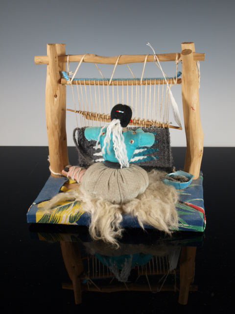 Vintage Navajo Doll, Rug Weaver At Her Loom: Handmade Navajo doll depicting a Navajo woman in traditional garb seated at a loom, weaving a rug with her infant laying next to her. Dimensions: 8 & 1/2 in. high x 9 & 1/4 in. wide x 5 & 1/2 in. deep
