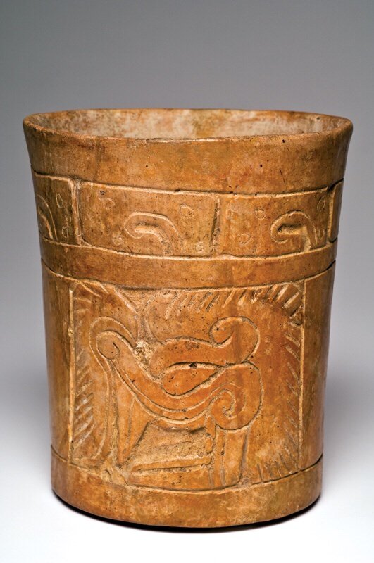 Maya Carved and Burnished Cylinder: The Mayan Areas - Classic MayaCulture or Country: El Salvador type.Period: Ca. 600-800 A.D.Size:6-1/2”H., 5-5/8”D.Description:Tan-brown pottery cylinder having a carved upper band containing seven