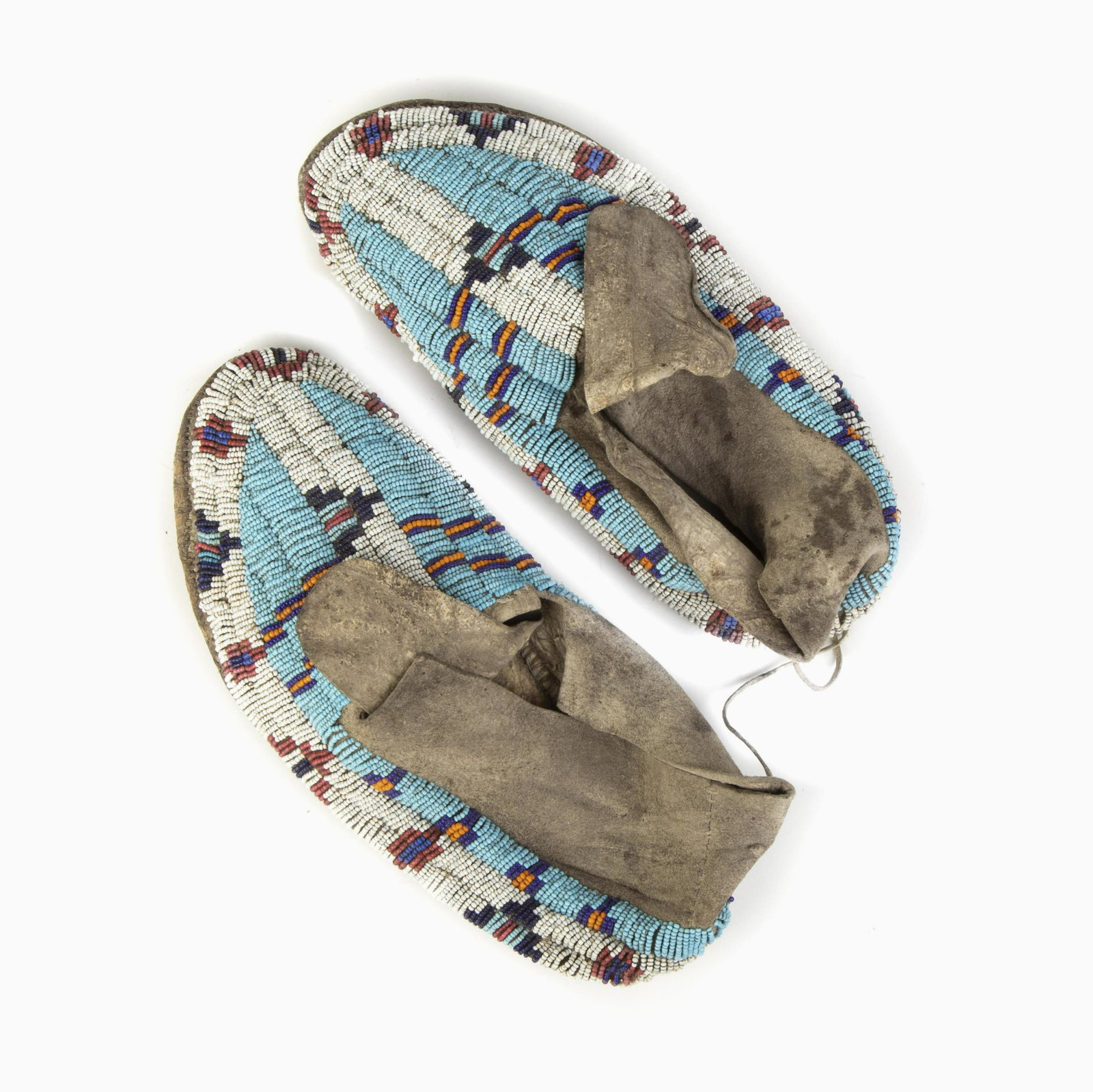 A Pair of Plains Beaded Hide Moccasins, ca. 1890: Plains A Pair of Beaded Hide Moccasins, ca. 1890 having light blue, dark blue, orange, white, and red glass seed beads rawhide soles Each: 10 1/4 x 4 1/4 x 3 1/4 in. (26.04 x 10.80 x 8.26 cm.) Private