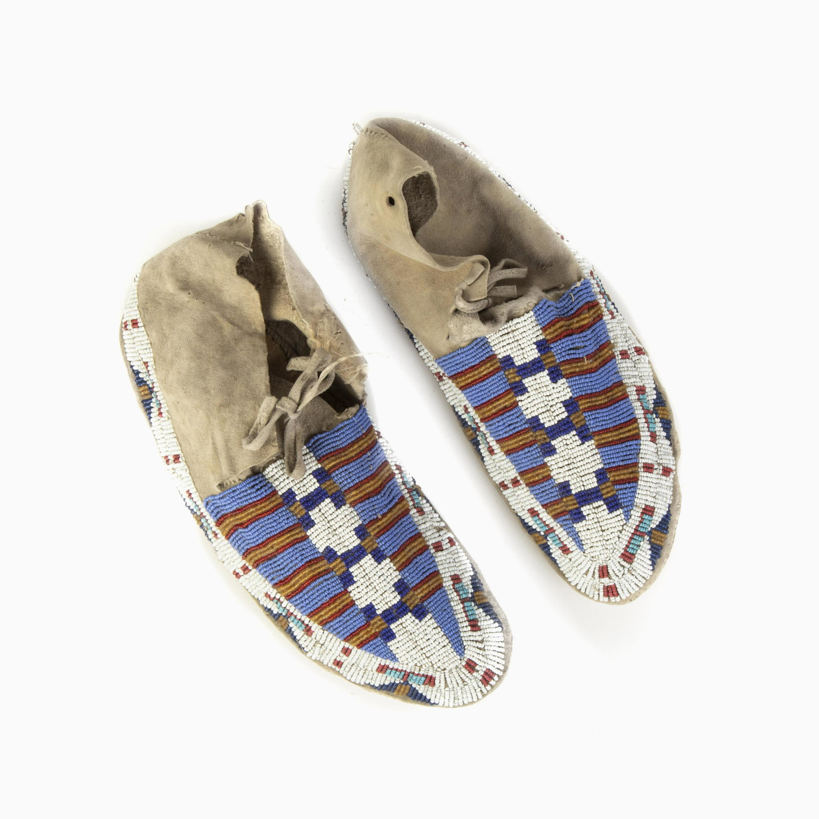A Pair of Plains Beaded Hide Moccasins, ca. 1920: Plains A Pair of Beaded Hide Moccasins, ca. 1920 having white, red, yellow, light blue, dark blue, purple, and pink glass seed beads rawhide soles Each: 10 x 3 3/4 x 3 5/8 in. (25.40 x 9.53 x 9.21 cm.